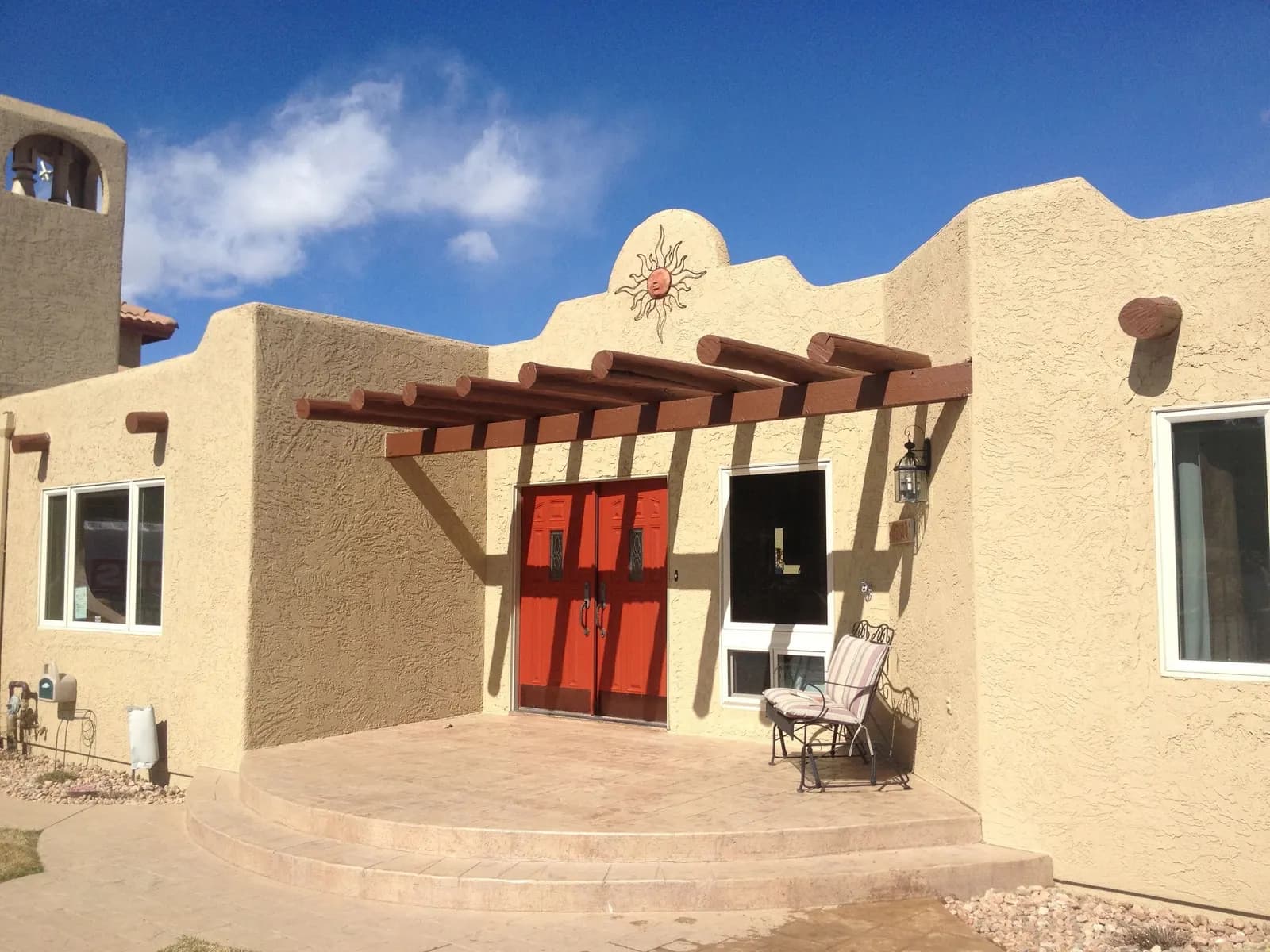 Tan stucco Southwest-style home with a wood pergola and red double front doors